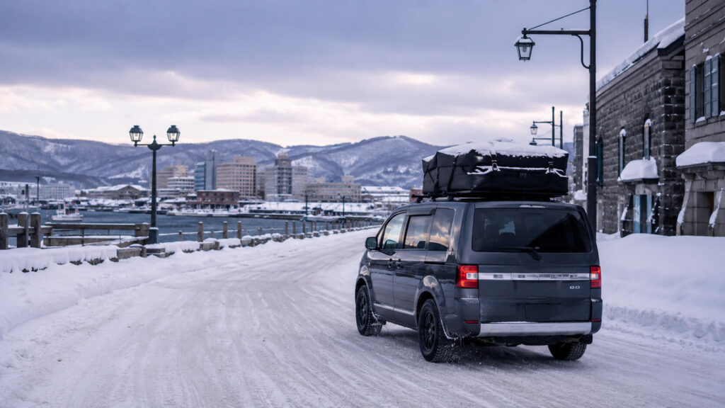 冬の小樽を走る車中泊仕様の車、雪道と港町の景色、防寒対策のイメージ